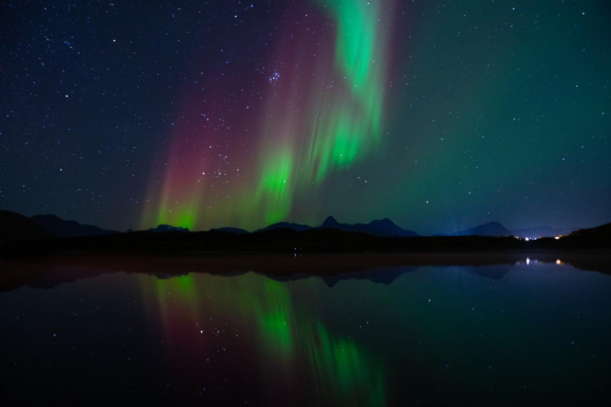 nordlys over m&oslash;rke fjell og en fjord